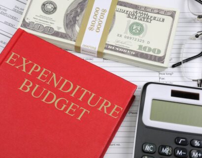 a red notebook with titles expenditure budgets, a dollar heap and calculator