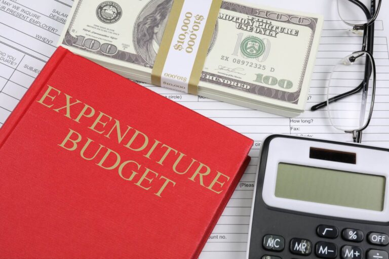 a red notebook with titles expenditure budgets, a dollar heap and calculator
